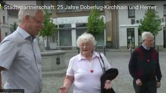 Drei ältere Personen stehen auf einem Platz mit Brunnen in Doberlug