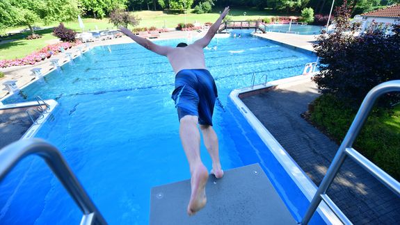Ein Jugendlicher macht einen Kopfsprung vom Sprungbrett des Freibads